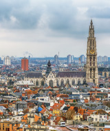 Vista de la ciudad de Amberes con iglesias históricas y edificios modernos bajo un cielo nublado.