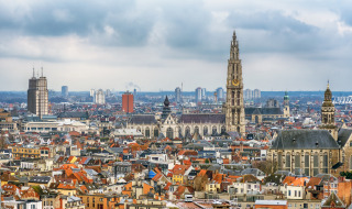 Skyline van Antwerpen met historische kerken en moderne gebouwen onder een bewolkte lucht.