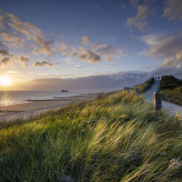 Puesta de sol junto al mar en un parque vacacional con glamping, dunas de césped y camino de arena.