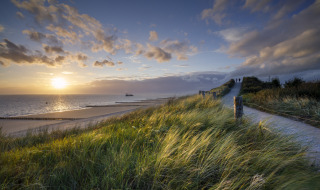 Puesta de sol junto al mar en un parque vacacional con glamping, dunas de césped y camino de arena.