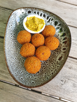 A stylish plate with seven crispy fried balls and a dish of yellow mustard dip on a wooden table.