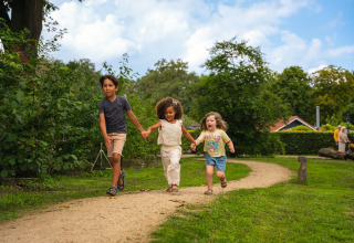 Drie kinderen rennen hand in hand op een wandelpad in het groene vakantiepark Sandberghe, Noord-Brabant.