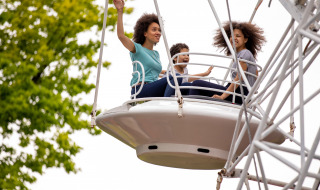 Three smiling people enjoy a Ferris wheel ride at a holiday park with glamping, surrounded by leafy trees.