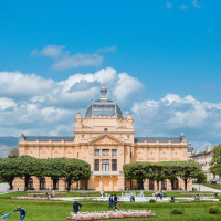 Monumentaal gebouw met glazen koepel, groene tuinen en mensen die genieten van een zonnige dag.