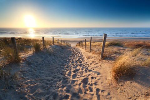 Solnedgang ved stranden nær Overveen, Nordholland, med sandsti, klitter og fredelige bølger.