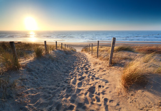 Puesta de sol en la playa cerca de Overveen, Holanda Septentrional, con sendero de arena y dunas.