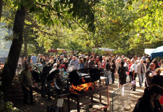 Een drukbezochte buitenbarbecue in een bosrijke omgeving tijdens een evenement op Camping le Rotja.
