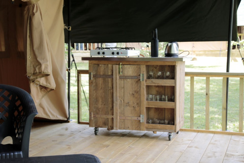 Cocina de té al aire libre en tienda safari con encimera de madera, cocina, hervidor y vasos en Camping le Rotja, Francia.