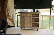 Cocina de té al aire libre en tienda safari con encimera de madera, cocina, hervidor y vasos en Camping le Rotja, Francia.