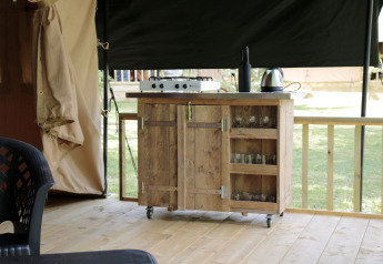 Cocina de té al aire libre en tienda safari con encimera de madera, cocina, hervidor y vasos en Camping le Rotja, Francia.