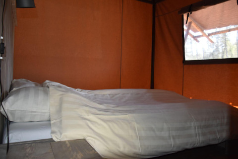 Cama acogedora con sábanas blancas en Veluwe Lodge en Camping Samoza, Países Bajos, ventana al fondo.