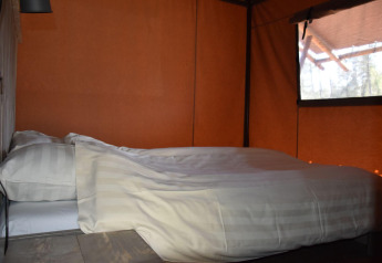 Cama acogedora con sábanas blancas en Veluwe Lodge en Camping Samoza, Países Bajos, ventana al fondo.