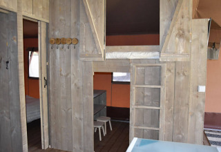 Interior de la Veluwe Lodge en Camping Samoza, Países Bajos, con cama elevada, muebles de madera y ambiente acogedor.