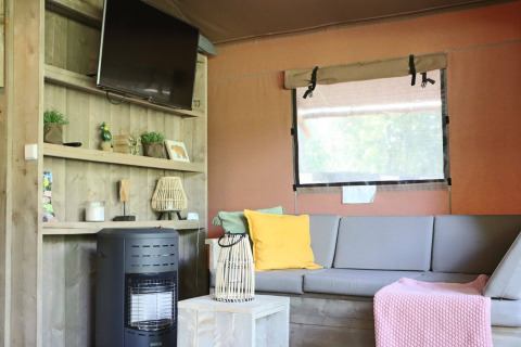 Sala con sofá gris, TV y estufa en Veluwe Lodge de Camping Samoza, Países Bajos.
