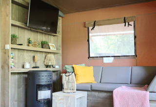 Sala con sofá gris, TV y estufa en Veluwe Lodge de Camping Samoza, Países Bajos.