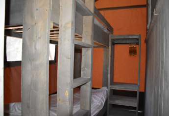 Litera de madera y armario abierto en una habitación compacta en Veluwe Lodge, Camping Samoza, Países Bajos.
