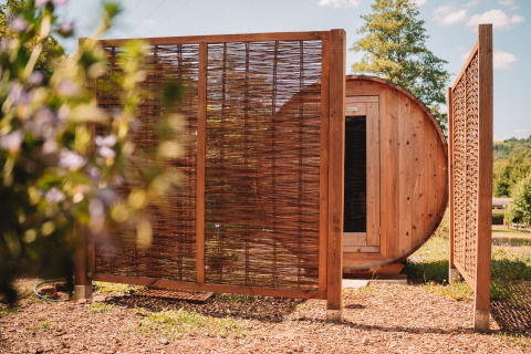Sauna de madera y pantalla de privacidad junto a tienda safari en Camping Donnersberg, Alemania, en verano.