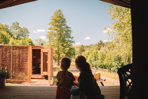 Two people enjoy the view from a safari tent with sauna at Camping Donnersberg, surrounded by greenery.