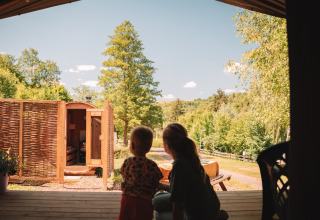 Two people enjoy the view from a safari tent with sauna at Camping Donnersberg, surrounded by greenery.