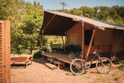 Safari tent with porch, bicycle, and outdoor dining at Camping Donnersberg, Germany, on a sunny day.