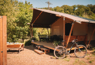 Safari tent with porch, bicycle, and outdoor dining at Camping Donnersberg, Germany, on a sunny day.