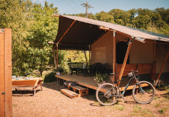 Safari tent with porch, bicycle, and outdoor dining at Camping Donnersberg, Germany, on a sunny day.