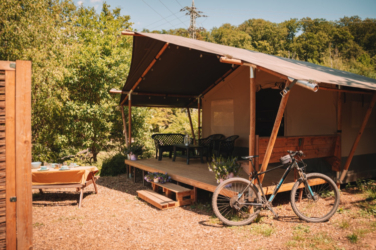 Tienda safari con porche, bicicleta y área de comedor al aire libre en Camping Donnersberg, Alemania.