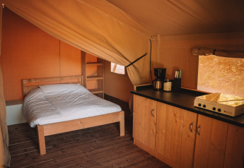 Interior de una tienda safari con cama doble, suelo de madera y cocina con cafetera y utensilios.