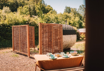 Außenbereich eines Safari-Zelts mit Sauna und gedecktem Tisch im Camping Donnersberg, Deutschland.