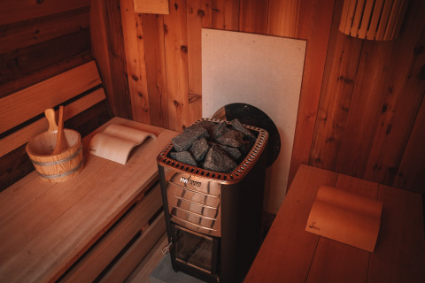 Interior view of a sauna with wooden benches, stove, and bucket inside Safari tent at Camping Donnersberg.