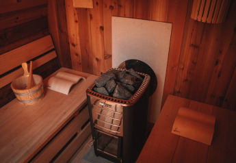 Vue intérieure d’un sauna avec bancs en bois, poêle et seau dans une tente Safari au Camping Donnersberg.