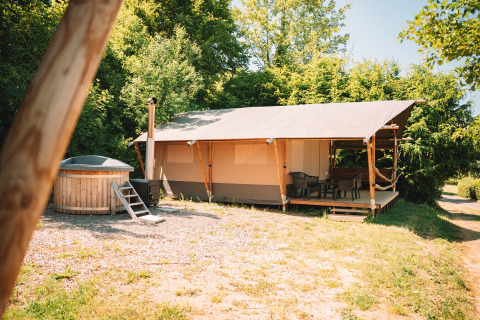 Tente safari avec terrasse en bois et bain à remous extérieur privé, entourée d'arbres et ciel dégagé.