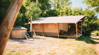 Tenda safari con veranda in legno e vasca idromassaggio privata, immersa tra alberi e cielo aperto.