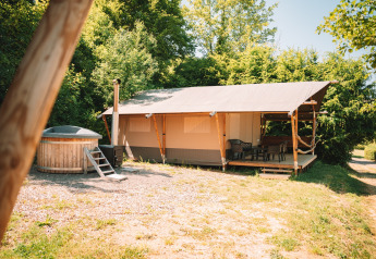 Tente safari avec terrasse en bois et bain à remous extérieur privé, entourée d'arbres et ciel dégagé.
