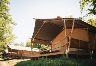 Grandes tiendas safari con estructuras de madera y porches en un camping rodeado de árboles verdes.