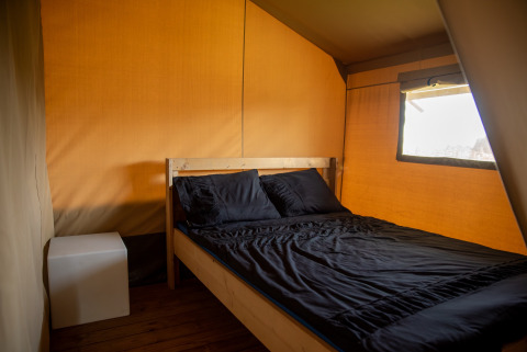 Interior de la tienda Safari en Camping de Boomgaard, Bélgica, con cama de madera y sábanas negras.