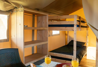 Vista interna di una tenda safari a Camping de Boomgaard con letti a castello e colazione apparecchiata.