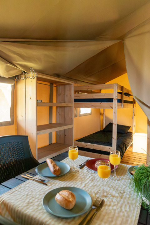 Binnenaanzicht van een safaritent bij Camping de Boomgaard met stapelbedden en ontbijt op tafel.