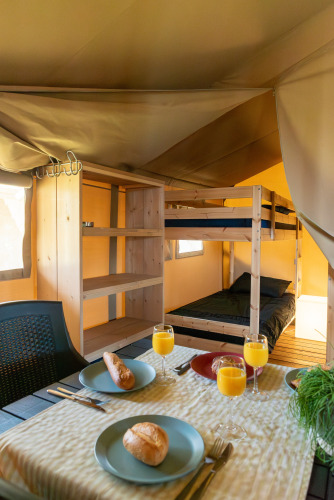 Vista interior de una tienda safari en Camping de Boomgaard con literas y desayuno servido en la mesa.