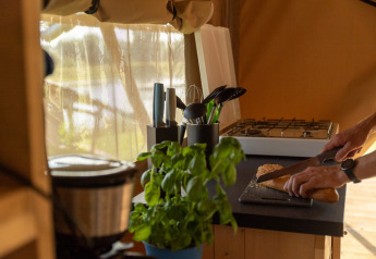 Interno della tenda safari Maaszicht al Camping de Boomgaard, una persona affetta il pane in cucina.
