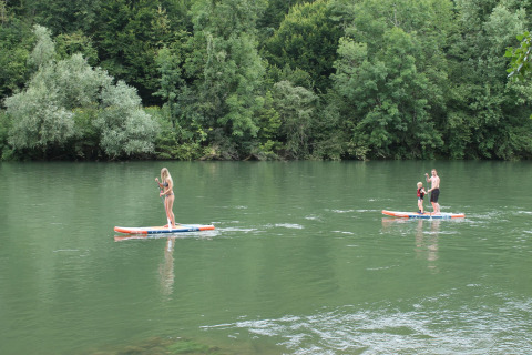 Three people paddle boarding on a calm river surrounded by lush greenery at Camping Sretanwolf in Croatia.