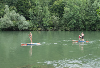Three people paddle boarding on a calm river surrounded by lush greenery at Camping Sretanwolf in Croatia.
