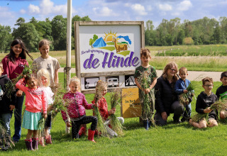 Kinderen en volwassenen poseren voor een bord van Boerderijcamping de Hinde in Flevoland, Nederland.