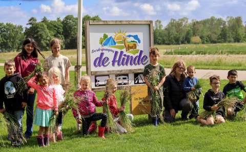 Kinderen en volwassenen poseren voor een bord van Boerderijcamping de Hinde in Flevoland, Nederland.