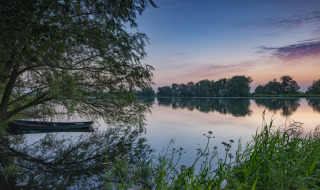 Tranquil lake scene near Dronten, Flevoland, Netherlands, with boat, trees, and reflections at sunset.