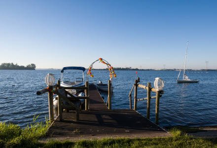 Steg mit Blumenbogen und Booten auf einem See, aufgenommen an einem Glamping-Urlaubsort bei Sonnenschein.