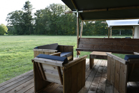 Houten tuinmeubilair op een overdekt terras met uitzicht op een groene open weide bij Safari tent + sanitair, Mooirust, Nederland.