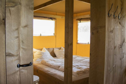 Binnenaanzicht van een gezellige slaapkamer in een safaritent met raam, hout en donzen beddengoed.