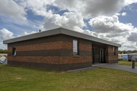 Modern brick building at Camping Jagtveld holiday park in South Holland, Netherlands, with cloudy sky.