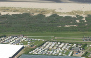 Luftfoto af Camping Jagtveld feriepark i Sydholland, Holland, med campingvogne nær strand og klitter.